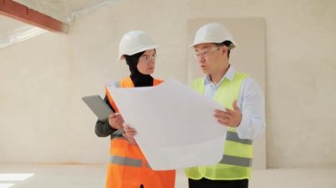 Çinli erkek emlakçı, Müslüman Arap iş kadınlarına ait boş dairenin planlarını gösteriyor. Erkek mühendis, bir otel ya da apartman projesi satın alma konseptini gösteriyor.