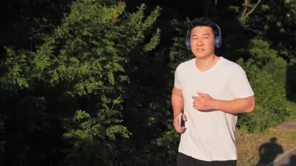 アジアのスポーツマンJog Cardio Workout Sunset携帯電話を持つ音楽を聴く マラソン競技前のランナーのフィットネスハードトレーニング 公園でランニングマンアスリートジョギング — ストック動画