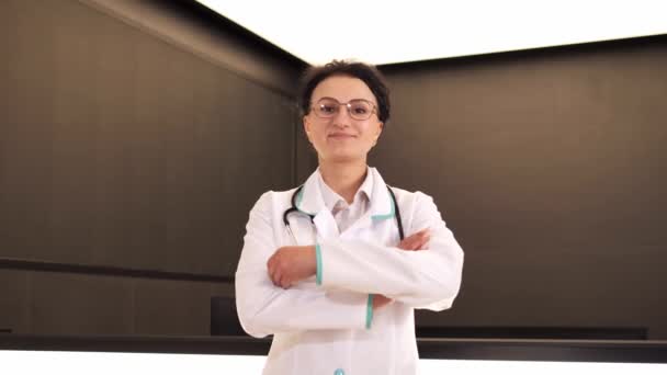白い医療コートとカメラを見て聴診器を身に着けている幸せなプロの女性医師 病院でポーズをとる女性医師の笑顔 積極的な一般開業医クローズアップ顔の肖像画 — ストック動画
