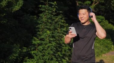 Sunset 'teki eğitimden sonra New Smartphone Run uygulamasını kullanarak, müzik dinleyen, kablosuz kulaklık takan mutlu Çinli sporcu. Kardiyo çalışması. Koşan Adam Spor Salonu