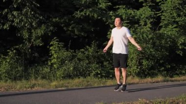 Güçlü Asyalı sporcu gün batımında ip atlayıp dışarıda idman yapıyor. Adam ip atlıyor. Açık hava üzerinde kardiyo çalışması. Hızlı kilo vermek için egzersiz. Atlama egzersizleri yapan bir dövüşçü.