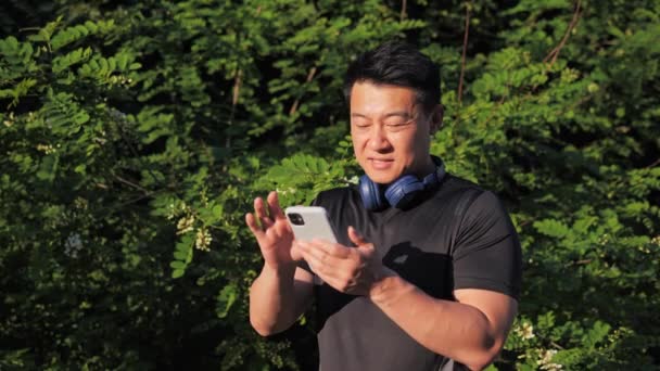 Szczęśliwy Koreańczyk Stojący Parku Pomocą Aplikacji Mobilnej Uśmiech Kończący Trening — Wideo stockowe