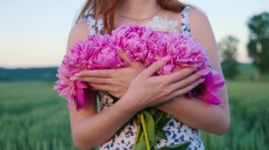 Çok çekici kızıl saçlı, kızıl saçlı genç bir kız. Pembe çiçekli bir kadın Tarlada yürüyor Özgürlüğün tadını çıkarıyor Büyüleyici bir gülüşü var Gün batımındaki yeşil buğday tarlasının