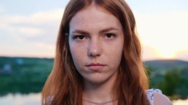 Kendine güvenen Hayalperest Surat Güzel Kızıl Saçlı Genç Kız Gün Batımında Doğanın Arkasında Poz Veriyor. Doğal Çocuk Güzelliği. Kadının uzun kızıl saçı var, çilli. Kahverengi gözlü. Açık hava.