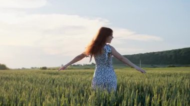 Neşeli kızıl saçlı, çilli, yaz elbisesi giymiş gün batımında dans eden mutlu kız. Güzel kızıl kadın atlarken eğleniyor doğa temiz havanın tadını çıkarıyor. Güzel manzara, yaz