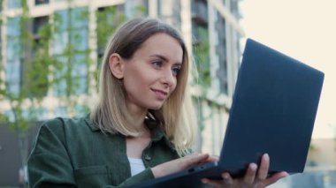 Neşeli, genç ve güzel bir iş kadını laptopuyla ofis merkezinin önünde duruyor. İnternetten mesaj yazıyor, internet bağlantısı kuruyor, teknoloji işi ağır çekimde çalışıyor.