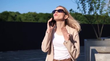 Güneş gözlüklü genç sarışının kadın portresi dışarıda duruyor ve cep telefonuyla el sallayarak öfkeli bir şekilde konuşuyor. Öfkeden kudurmuş kız kavgası kötü sözler söylüyor duygusal suistimal..