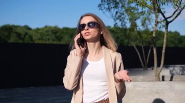 Başarılı sarışın iş kadını dışarıda cep telefonuyla konuşuyor. İş kadını sokakta yürürken cep telefonuyla konuşuyor. Konuşan güzel bir kadın profesyonel.