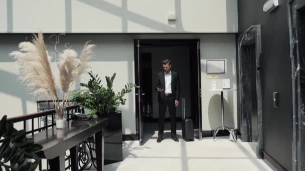 Ελκυστικός Επιχειρηματίας Που Στέκεται Στο Διάδρομο Του Ξενοδοχείου Χρησιμοποιώντας Την — Αρχείο Βίντεο