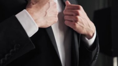 Bir adam pencerenin önünde duruyor ve iş toplantısına gidiyor. İnsanın yakın görüntüsü elbisesini ayarlar. İşadamı sabah rutininde takım elbise giydi, işe gitmeye hazırlanıyordu.