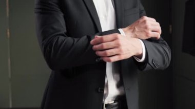 Kendine güvenen genç adam oteldeki siyah takımı ayarlıyor iş toplantısına hazırlanıyor, kollarını kavuşturuyor ve iş gezisi sırasında otel odasında poz veriyor.