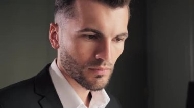 Portrait of young elegant business man posing at dark office near window. Closeup gorgeous man face smiling at camera indoors. Rich charming businessman looking posing to camera inside hotel room