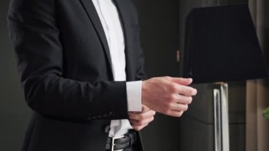 Stylish businessman in formal suit straightens the cuffs of his jacket in hotel room during business trip. The man is going to a meeting in the morning indoor