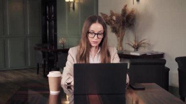 Beautiful stylish businesswoman in eyeglasses using laptop working in hotel room remotely on her business travel. Business woman working on laptop in restaurant. Lady sitting in chair with notebook