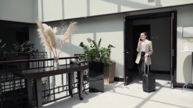 Resmi takım elbise giyen ciddi bir iş kadını otel odasında cep telefonuyla iş konuşuyor. Modern cihazlar, iletişim ve gidip gelen yaşam tarzı seyahat kavramı