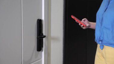 Mavi elbiseli bir iş kadını modern bir otelde kapıyı açmak için cep telefonu uygulaması kullanıyor. Kız, en son iletişim sistemini kullanarak kapıyı açıyor. Otel işletme teknolojileri