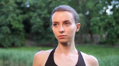 Başını Gülümseyen ve Park 'ta Duran Mutlu Genç Güzel Sporcu Kızın Portresi. Kadınların atletik yüzünü kapatın. Neşeli Kadın Spor Antrenörü Dışarıda Kameraya Bakıyor