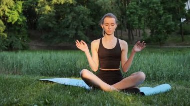 Güzel bir kadın, yeşil ağaçlar üzerinde Lotus pozisyonunda yoga meditasyonu yapıyor. Sağlıklı dişi kız nilüfer çiçeği pozisyonunda oturur ve dışarıda yoga yapar, dinlenir.