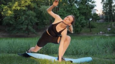 Sıska Atletik Sarışın Kadın Gün Batımında Bir Yatakta Oturarak Isınıyor. Açık hava sporu, formda sporcu kadın dışarıda antremandan önce vücudunu ısıtıyor. Akşam egzersizleri sağlık içindir.