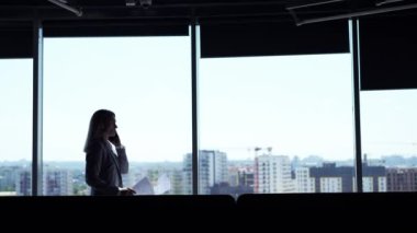 Silhouette of businesswoman using smartphone chatting to client financial advisor negotiating business deal corporate sales phone call girl walking along hall of building with panoramic windows