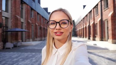 Genç çekici kadın blogcu veya vlogger, kanal için içerik videosu kaydediyor ve şehrin arka planıyla konuşan cep telefonu web kameralarına bakıyor. Neşeli kız video bağlantısıyla konuşuyor.