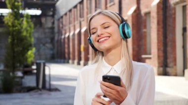 Mükemmel ciltli, güzel, mutlu bir kadın. Sağlıklı dişleri var. Kulaklık takıyor, sokaklarda cep telefonu uygulaması kullanıyor. Gülümseyen genç kız açık havada müzik dinliyor.