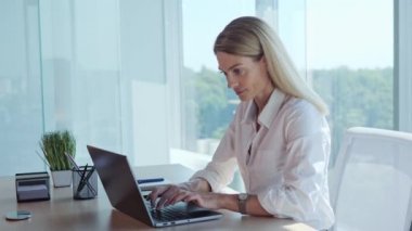 Smiling Professional blonde business woman in formal suit using laptop computer sits at workplace desk near window panoramic. Happy lady employee businesswoman executive working typing on pc in office