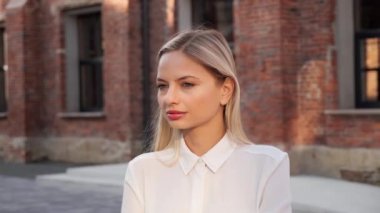Portrait of Smiling Beautiful Young Caucasian Blond Woman Standing in Urban Street. Pretty Business Lady with Blue Eyes White Healthy Teeth Attractive Appearance looking into Camera Outdoors