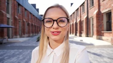 Beautiful woman blogger student is recording content video for channel and looking at mobile phone web camera talking with university background. Girl in eyeglasses talking via video link
