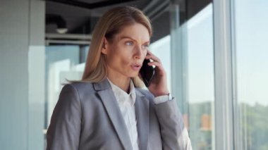 Concentrated businesswoman talking mobile phone in office. Serious manager portrait having smartphone conversation indoor. Business lady woman CEO solves the tasks. Successful company female leader