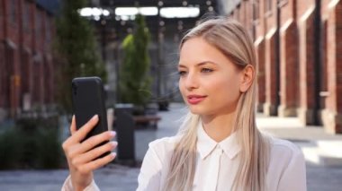 Close up portrait face caucasian blonde happy woman video chatting online on mobile phone outdoor. Joyful beautiful female recording vlog in street. Social media influencer. Communication concept