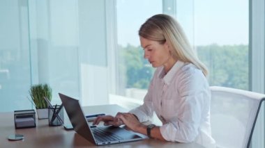 Side view of concentrated female employee suffer from severe pain in stomach at workplace. Young manager working on laptop standing near panoramic window having belly ache in office, menstruation