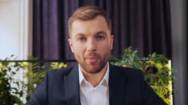 Happy serious business man, businessman talking to web cam on conference video call in restaurant. Smiling male coach talking, looking at camera during webinar, online virtual meeting, webcam view
