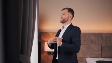 Confident businessman adjust modern dark suit near window in hotel room Handsome man wearing a nice suit. Businessman preparing go to meeting with business partner discuss the details of the contract