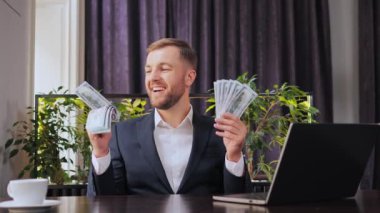 Happy businessman holding lots of money in hands, kissing dollars, made a profit or a win. Man rejoices in financial win holds fan of money sniffing Dollars satisfied with salary loan wealth success