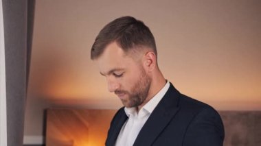 Elegant businessman adjust modern dark suit near window in hotel room Handsome man wearing a nice suit. Businessman preparing go to meeting with business partner discuss the details of the contract