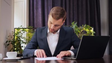 Focused business man entrepreneur typing on mobile phone using laptop doing analytics, research. Young male professional using documents sitting in restaurant. Busy worker freelancer working indoor