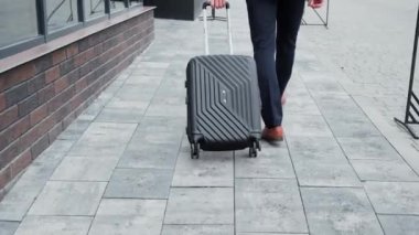 Traveling man with baggage settling in business hotel. Businessman arriving in hotel for business trip. Close up male legs walking to the hotel moving suitcase going to enter of reception desk