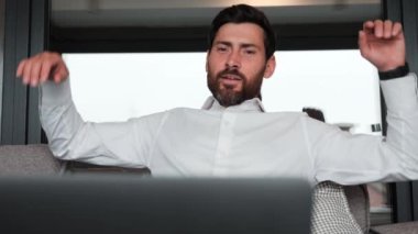 Businessman finishing working in luxury apartment. Bearded handsome business man worker relax sit at couch finished laptop work put hands behind head feel satisfied with work well done stress relief