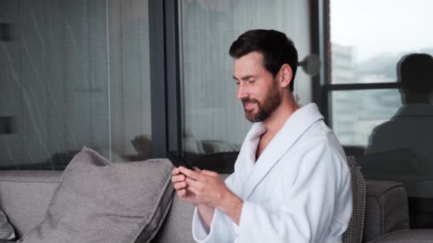 Bearded Happy Young Handsome Guy Bathrobe Sitting Sofa Home Using — Wideo stockowe