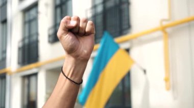 Close-up of a raised fist of person at a demonstration opposition against Russian aggression annexation of part of the territory of Ukraine. Peace in the world. Revolution, rebellion. Flag of Ukraine