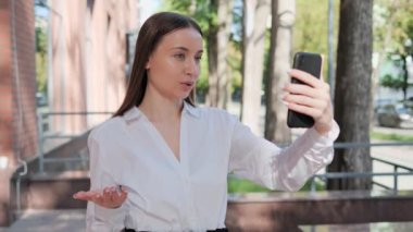 Neşeli, kendine güvenen, ciddi iş kadını videosu açık havada cep telefonuyla sohbet ediyor. Güzel bayan serbest çalışan sokakta akıllı telefon kullanarak video kaydediyor. Sosyal medya etkileyiciName