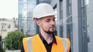 Kapalı çekimde gülümseyen mutlu mimarın portresi koruyucu miğfer ve yelek giymiş bir mühendisin başparmağıyla kameraya bakıp olumlu servis onayı veren dış mekan sembolü vermesi..