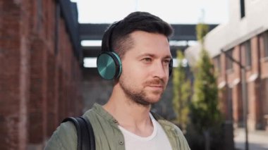 Mutlu pozitif adam serbest çalışan kulaklıklarını çıkarıyor. Güler yüzlü adam şehir sokağında dikiliyor kulaklıklarını çıkarıyor ve kameraya bakıyor. Adam müzik dinliyor, şehir gürültüsünden dinleniyor.