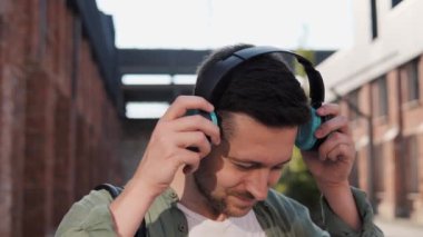 Serbest çalışan olumlu bir adam kablosuz yeşil kulaklık takıyor. Gülümseyen adam şehir sokağında durup kameraya gülümsüyor. Müzik dinleyen bir adam, kaliteli müzik dinlemekten hoşlanır.