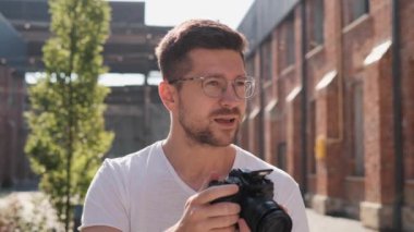 Neşeli yakışıklı erkek portresini yakın çekimde, keyifli bir ruh hali içinde ve şehirde kamerayla dikiliyor. Fotoğraf çeken mutlu bir turist. Fotoğrafçı fotoğraf çekiyor. Kentsel seyahat kavramı