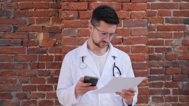 拿着智能手机打字或回复病人的严肃男医生 身穿白衣的男医生在室外窃听手机 医护专业人员远程为病人提供建议 — 图库视频影像