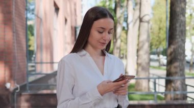 İş kadını dışarıda duruyor. Akıllı telefon kullanarak e-postaları kontrol ediyor.