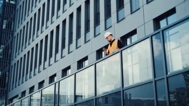 Profesyonel mimar mühendisi terasta duruyor ve cep telefonundan mesaj okuyor.