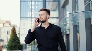 Siyah gömlekli genç iş adamı sokakta cep telefonuyla konuşuyor.